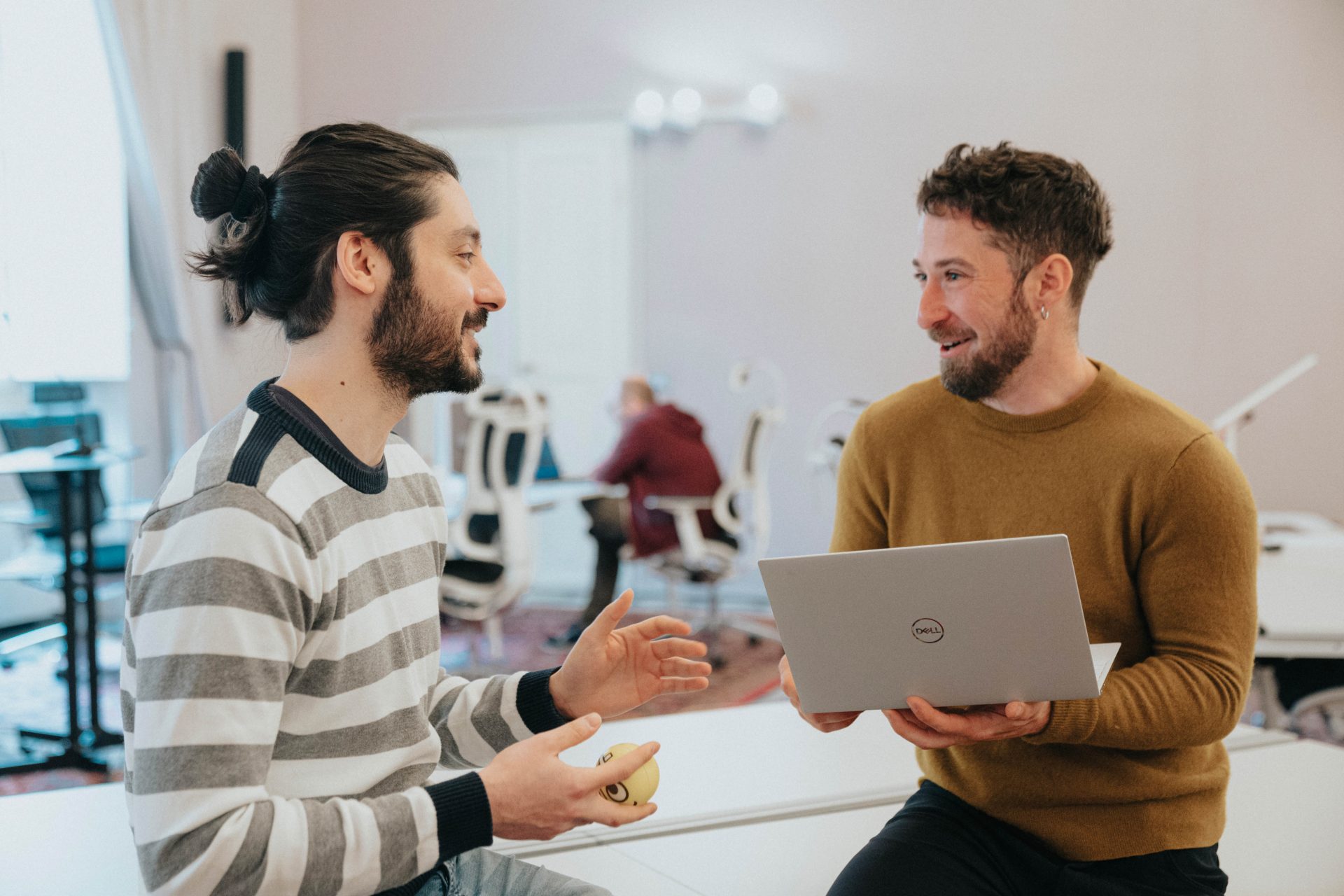 Due ragazzi che discutono di un progetto seduti in un salone di ufficio. Il ragazzo a destra ha un laptop aperto nelle mani.
